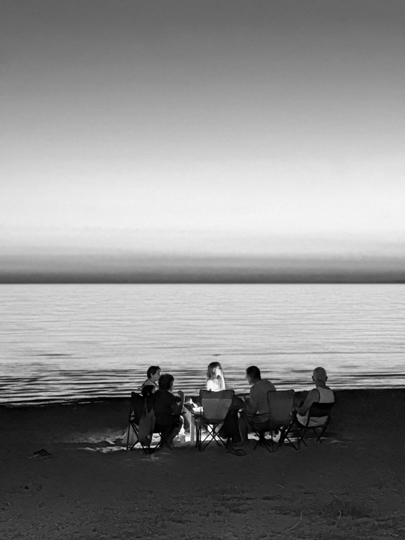 Un grupo conversa alrededor de una fogata frente al mar al anochecer
